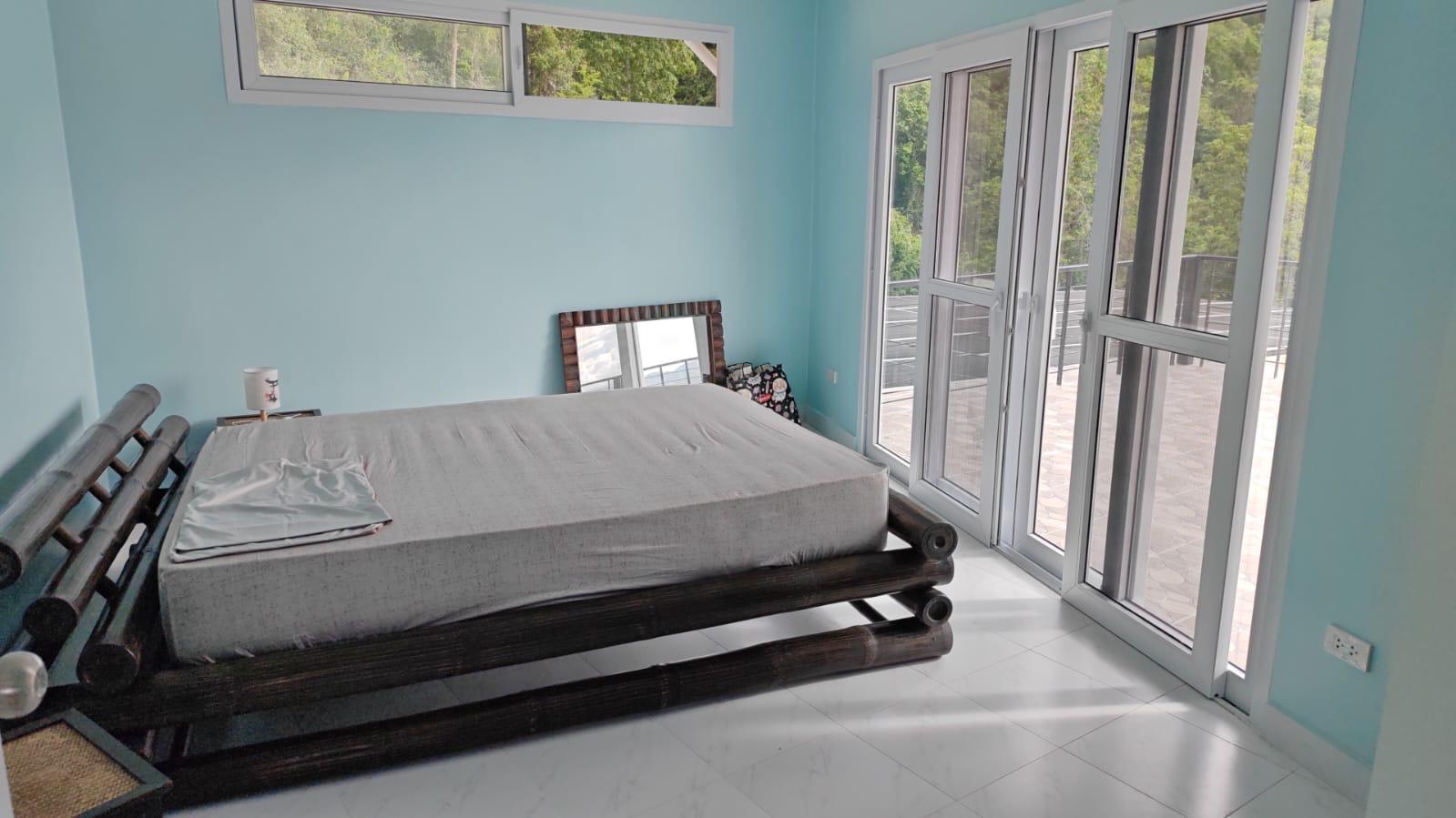Furnished bedroom with teal walls, bamboo bed frame and terrace access